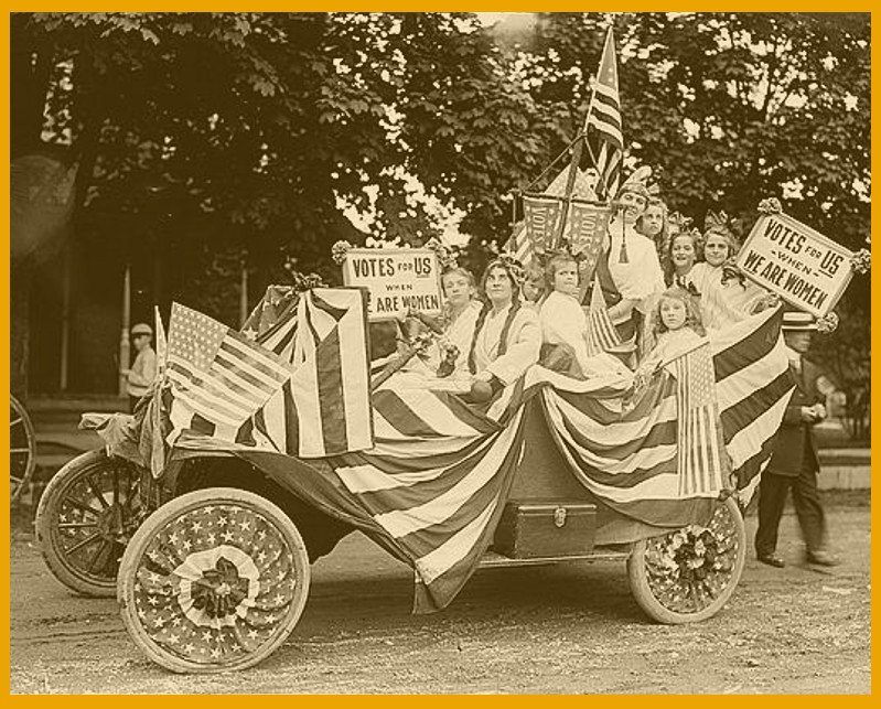 Flag-bedecked suffragists ride in a parade in a flag-bedecked automobile.