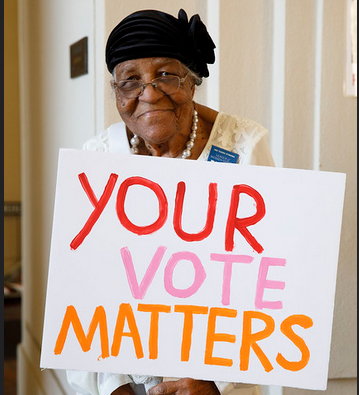 Photo of an adorable older lady holding a sign that says, 'Your Vote Matters'